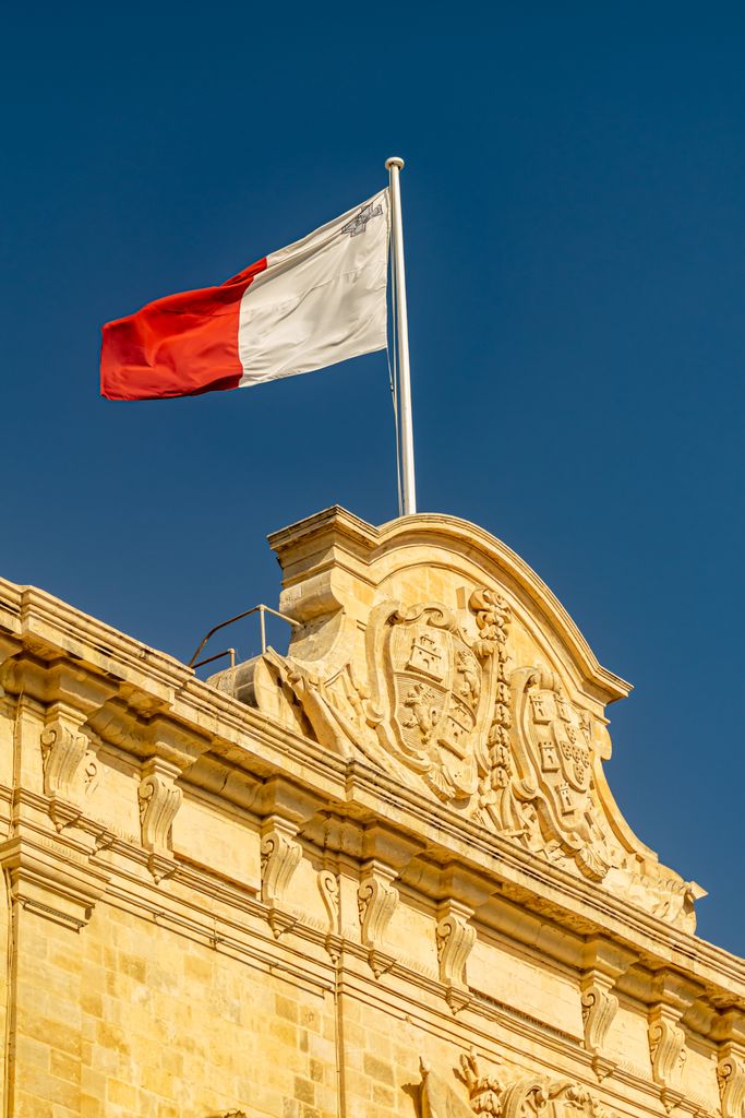Elegant historic Maltese building topped with the national flag under a clear blue sky.