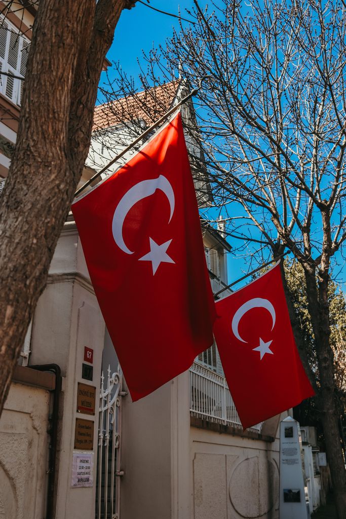 View of Turkish flags hanging in Heybeliada, Istanbul, with clear blue sky and trees.