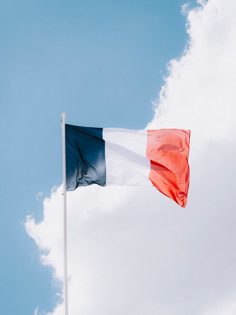 The French flag waving in the wind, set against a vibrant blue sky with clouds.