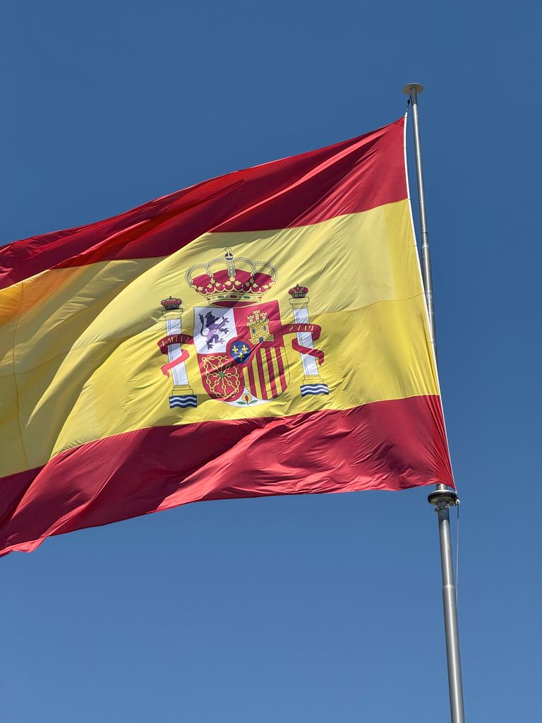 Vibrant Spanish flag fluttering against a bright blue sky, symbolizing national pride.